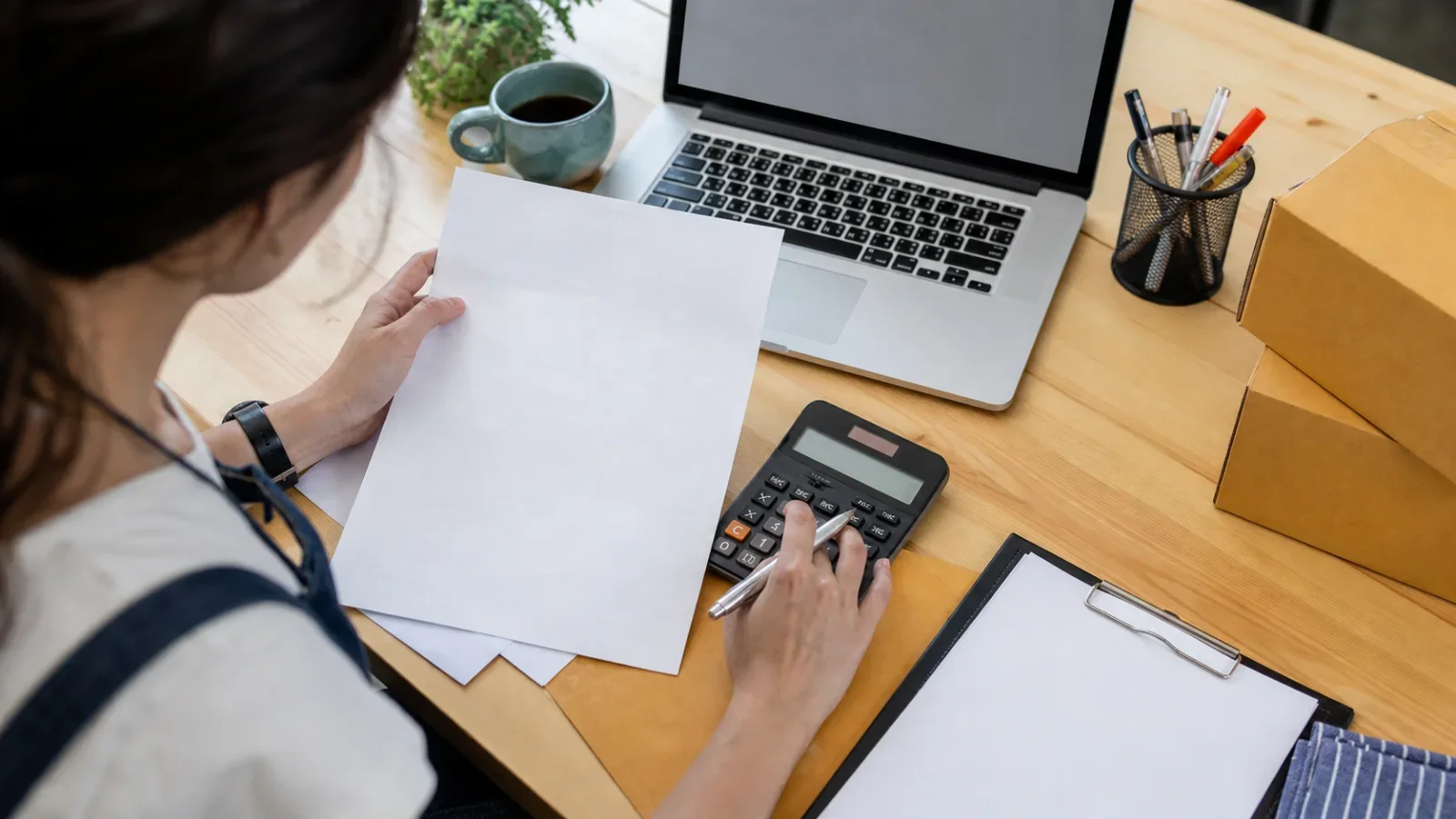 Vista superior de una persona calculando indicadores financieros sobre documentos del negocio.
